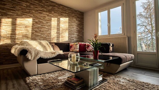 Un salon moderne avec un mur en pierre, une table basse en verre, un canapé et une vue sur l’extérieur.