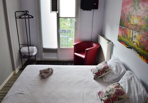 Une chambre d’hôtel avec un lit, une chaise rouge, un porte-manteau et un tableau au mur.