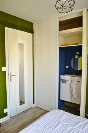 Un dormitorio con cama, una puerta blanca y un baño con lavamanos y espejo.