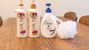 Tres botellas de crema Dove para el cuerpo y una esponja de baño blanca y mullida sobre una mesa de madera.