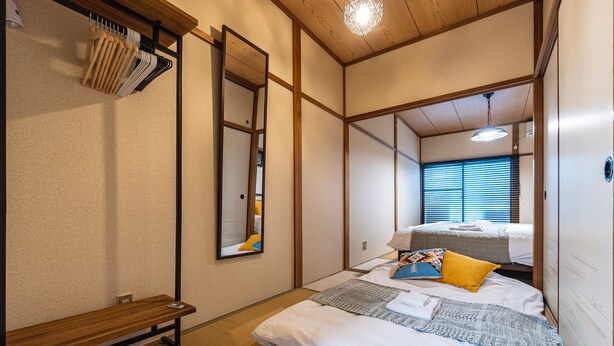 Una habitación tradicional japonesa con suelo de tatami, una cama de madera baja, un banco y un perchero con utensilios.