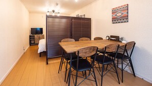Un área de comedor con una mesa de madera y sillas negras, un televisor al fondo y una obra de arte decorativa en la pared.