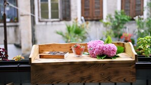 A wooden tray with a book, a glass container with a plant, and pink flowers on a balcony. - Vitopolis Apartment 3 (Rijeka)