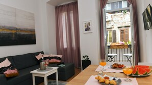 A living room with a sofa, a coffee table, and a breakfast table with food and drinks. - Vitopolis Apartment 3 (Rijeka)