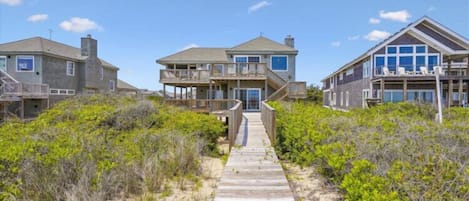 A beachfront property with a wooden pathway leading to a house with a balcony.