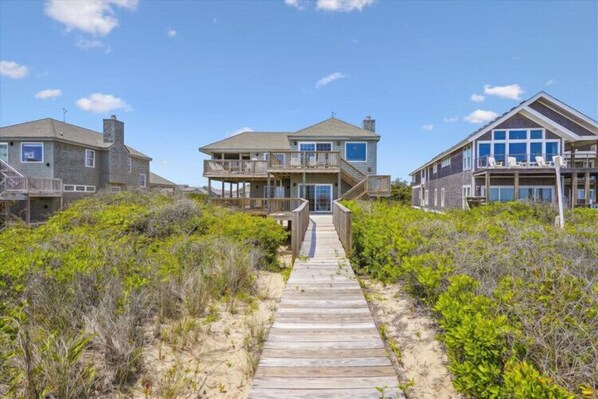 A beachfront property with a wooden pathway leading to a house with a balcony.