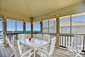 A covered outdoor patio with a table and chairs, overlooking a body of water. - Oceanfront at Ships Watch! (Duck)