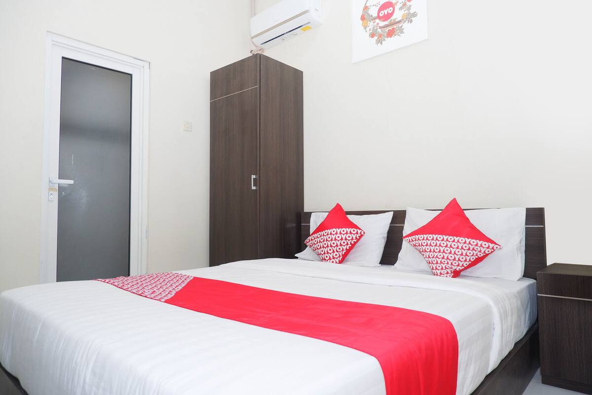 A hotel room with a bed, a wardrobe, and a wall-mounted air conditioner.