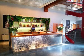 A bar area with a counter, shelves of bottles, and a decorative plant arrangement. - Hotel Fabrik (Humanes de Madrid)