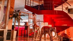 Un atrio de varios niveles con una llamativa escalera espiral roja, una zona de recepción con mostrador, y una escultura de jirafas y elefantes.