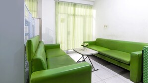 A room with a green sofa set, a small table with a vase of flowers, and a window with sheer curtains. - OYO 1242 Penginapan Rb Syariah (Depok)