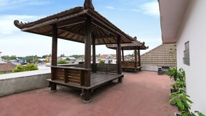 A wooden gazebo with a tiled roof, a bench, and potted plants on a rooftop terrace. - OYO 1242 Penginapan Rb Syariah (Depok)