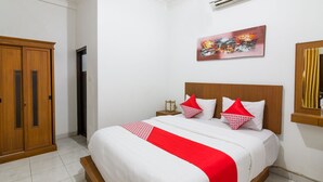 A neatly arranged bedroom with a large bed, a wooden wardrobe, a nightstand with a lamp, and a painting on the wall. - OYO 1242 Penginapan Rb Syariah (Depok)