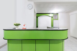 Un mostrador de recepción con una encimera verde, un reloj en la pared y una pequeña planta en maceta.