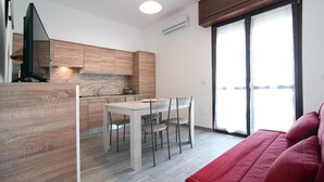 Eine moderne Küche mit Holzschränken, einem Esstisch mit Stühlen und einem roten Sofa in einem hellen Wohnbereich mit einem großen Fenster.