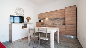 Eine moderne Küche mit Holzausstattung, einem Esstisch mit Stühlen, einem Flachbildfernseher und einer Wanduhr.