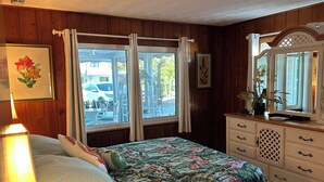 Une chambre à coucher avec un lit, une commode, un miroir et une fenêtre avec des rideaux.