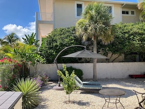 Une terrasse avec une table et des chaises, un petit parasol et un coin salon avec des coussins.