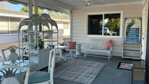 Un patio couvert aménagé avec des meubles en osier, un banc blanc agrémenté de coussins rouges et un panneau décoratif.