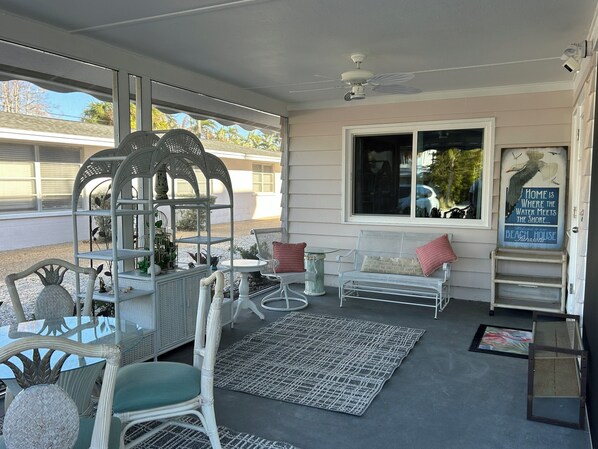 A covered patio area with wicker furniture, a white bench with red cushions, and a decorative sign.