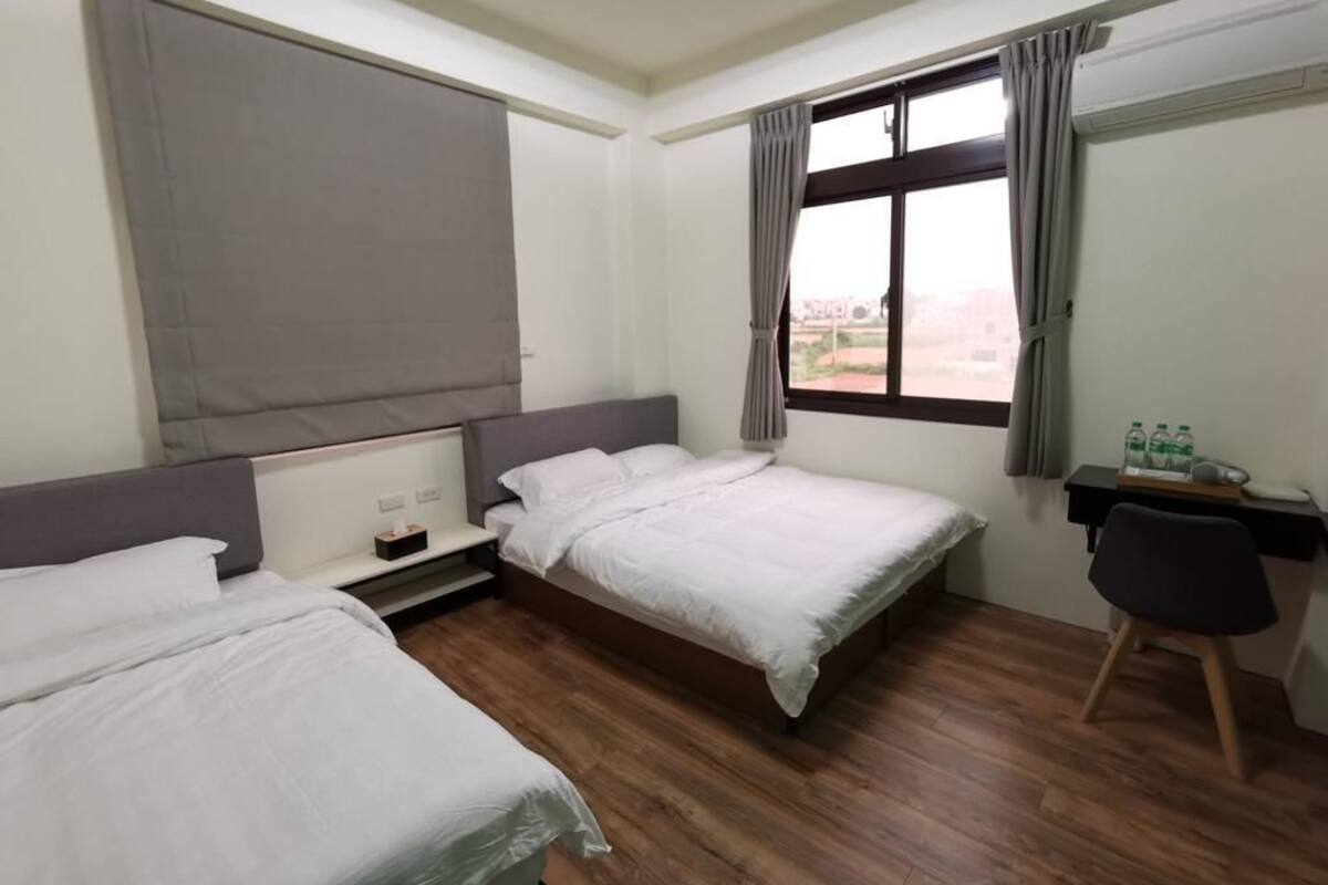 Habitación de hotel con dos camas individuales, un escritorio con silla, una ventana con cortinas y vistas al exterior.