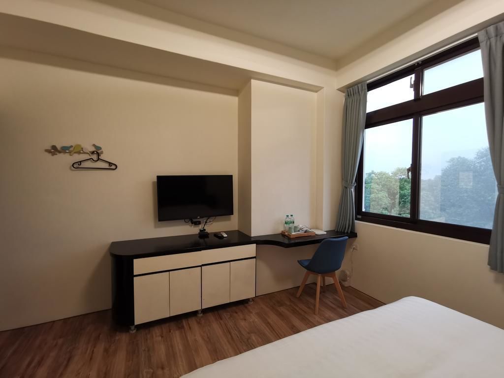 Habitació d'hotel amb un llit, escriptori amb cadira, televisió i finestra amb cortines.