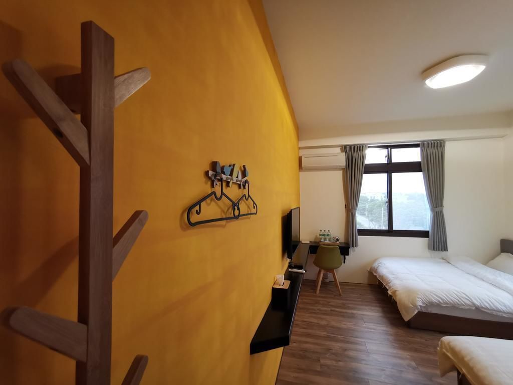 Habitación de hotel con estructura de madera a la izquierda, un escritorio con silla, dos camas y una ventana con cortinas.