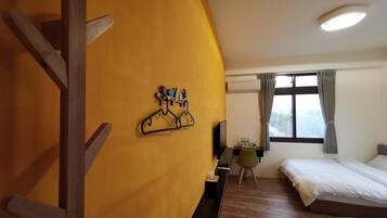 Habitación de hotel con estructura de madera a la izquierda, un escritorio con silla, dos camas y una ventana con cortinas.