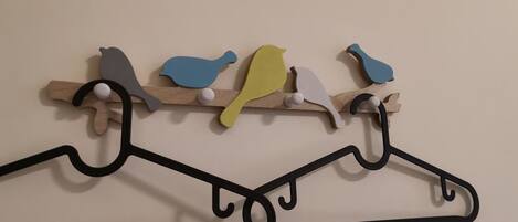 A wall-mounted wooden rack with colorful bird-shaped hooks and a black hanger below.