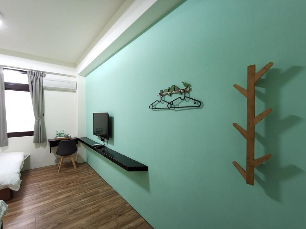 Una habitación con una cama, un escritorio con silla, un televisor y un perchero en la pared.