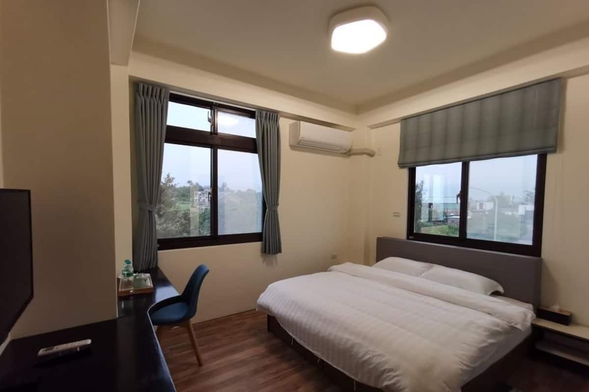 Una habitación de hotel con una cama, un escritorio, una silla y dos ventanas con cortinas.