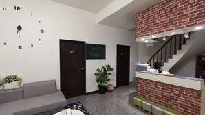 Un vestíbulo moderno con un sofá, una mesa de centro, un reloj, una escalera y un mostrador de recepción.