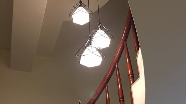 Una escalera con barandas de madera y una lámpara colgante geométrica.