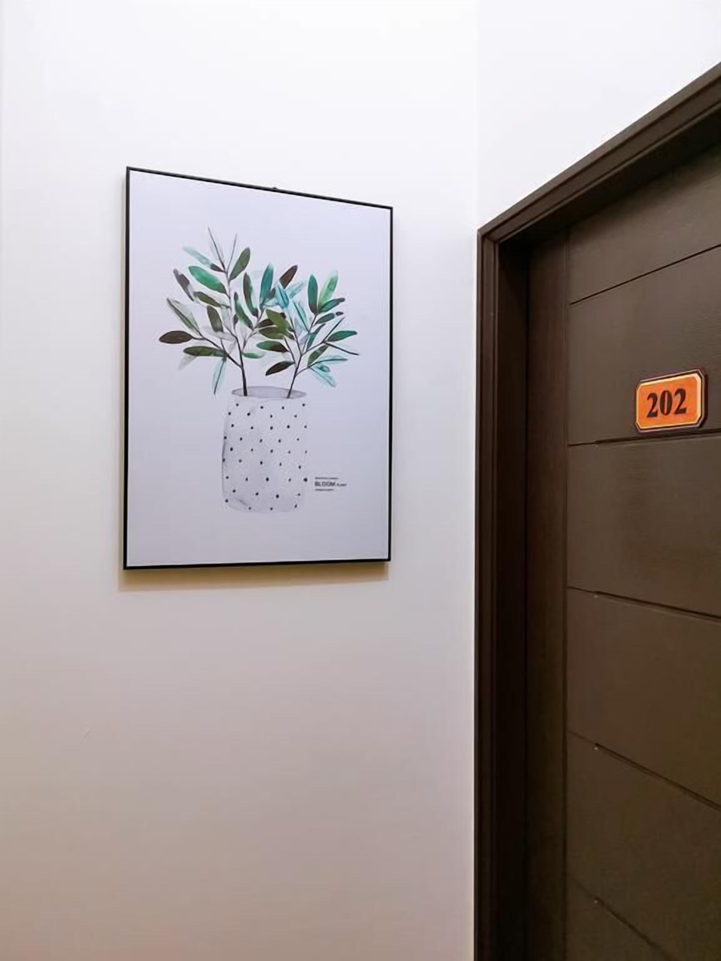 Una ilustración botánica enmarcada en una pared, junto a una puerta con una placa numérica.