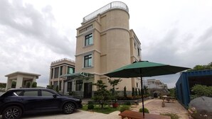 Un edificio moderno con fachada curva, un coche estacionado adelante y una mesa de picnic con sombrilla.