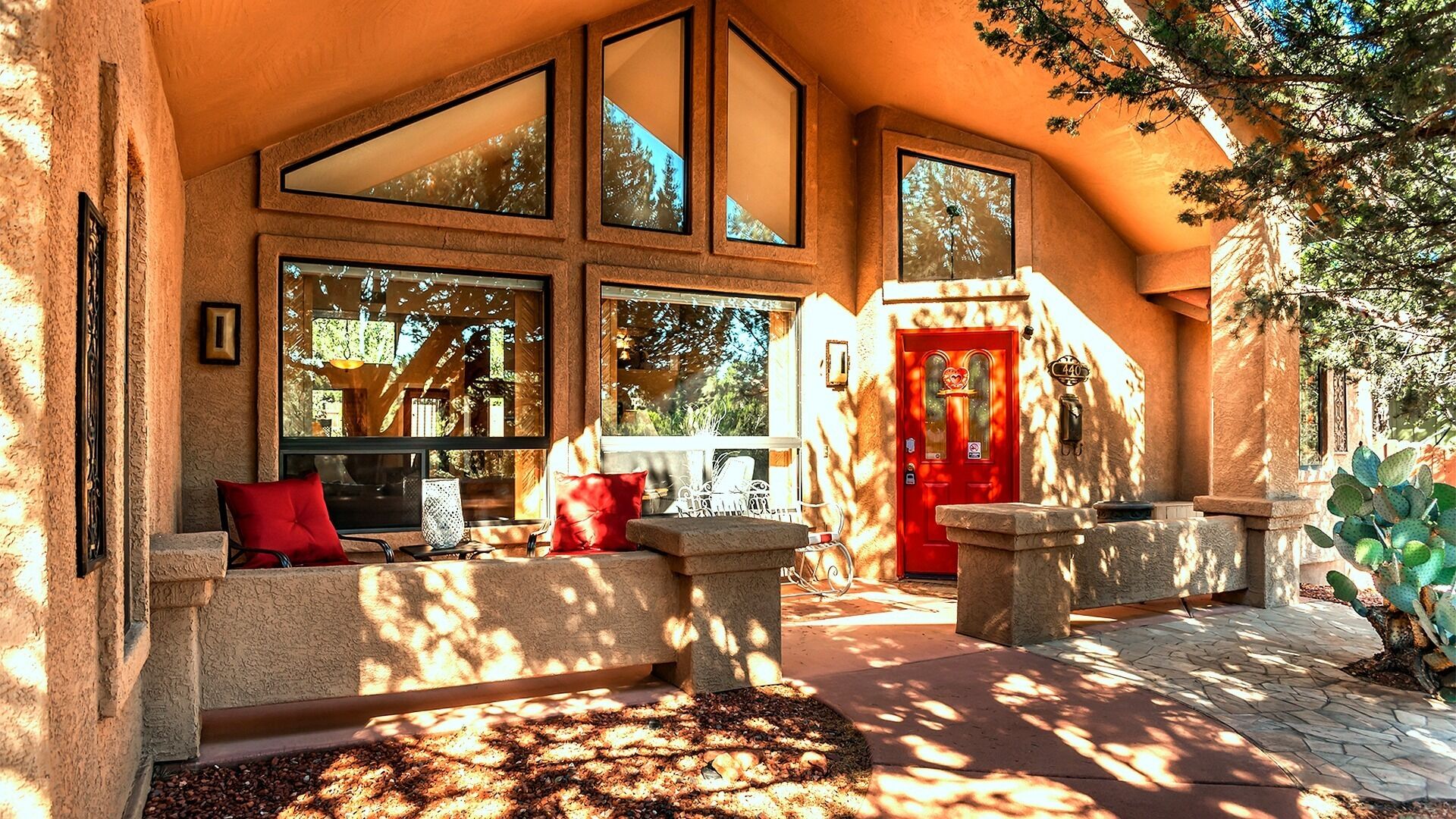 Un espacio exterior acogedor con bancos de piedra y cojines rojos, ventanas amplias y una puerta roja.