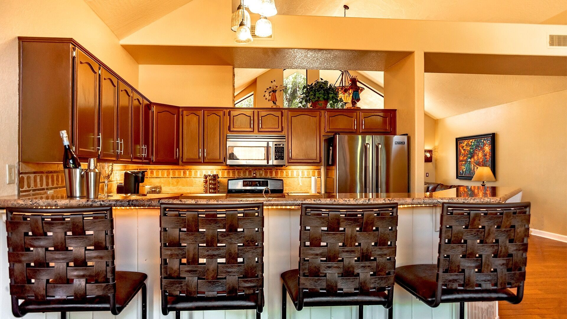 Una cocina con armarios de madera, electrodomésticos de acero inoxidable y una zona de bar con sillas de mimbre.
