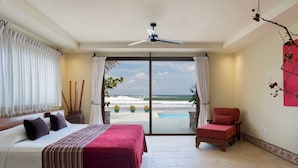 Ein Schlafzimmer mit Bett, Stuhl und Meerblick durch eine Schiebetür.