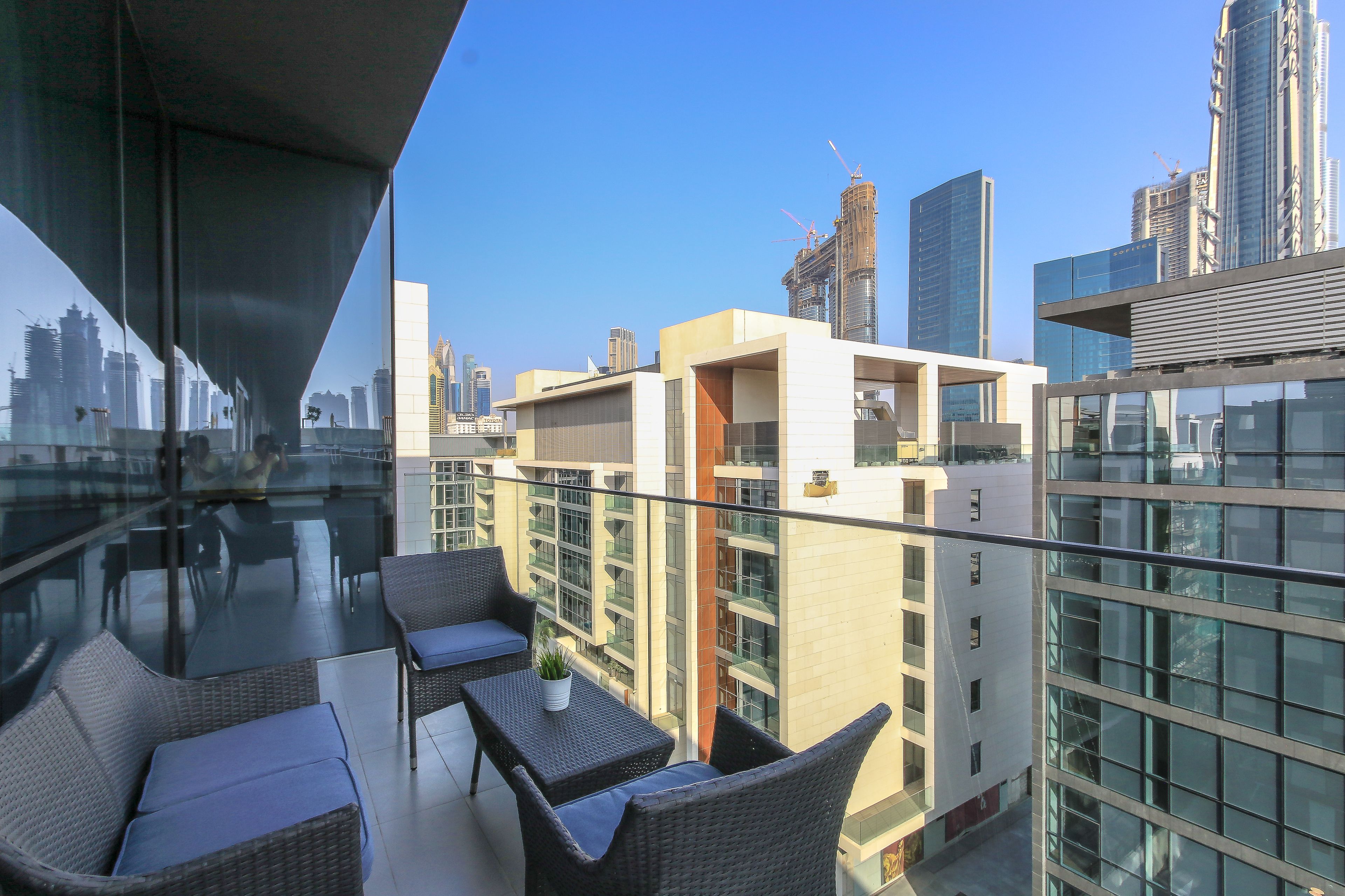 A balcony with wicker furniture, a glass table, and a view of the cityscape.