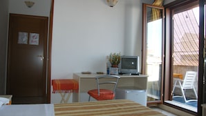 A hotel room with a bed, a desk with a computer, a chair, a small refrigerator, and a sliding glass door to the outside. - Oasi del Sud (Pozzallo)