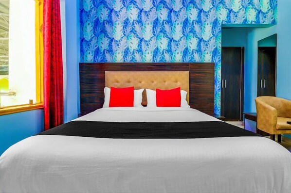 A hotel room with a large bed, red and white pillows, a wooden headboard, and a blue patterned wall. - Hotel The Grand Bhavya Palace (Basti)