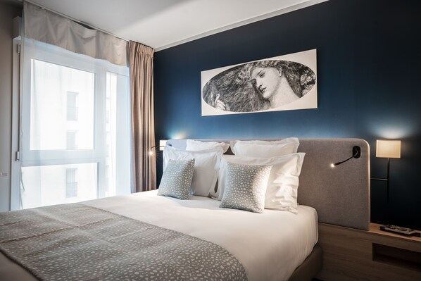 A neatly made bed with a patterned bedspread and pillows, a headboard with a light switch, a wall-mounted artwork, and a bedside table with a lamp. - Residhome Saint Ouen (Saint-Ouen)
