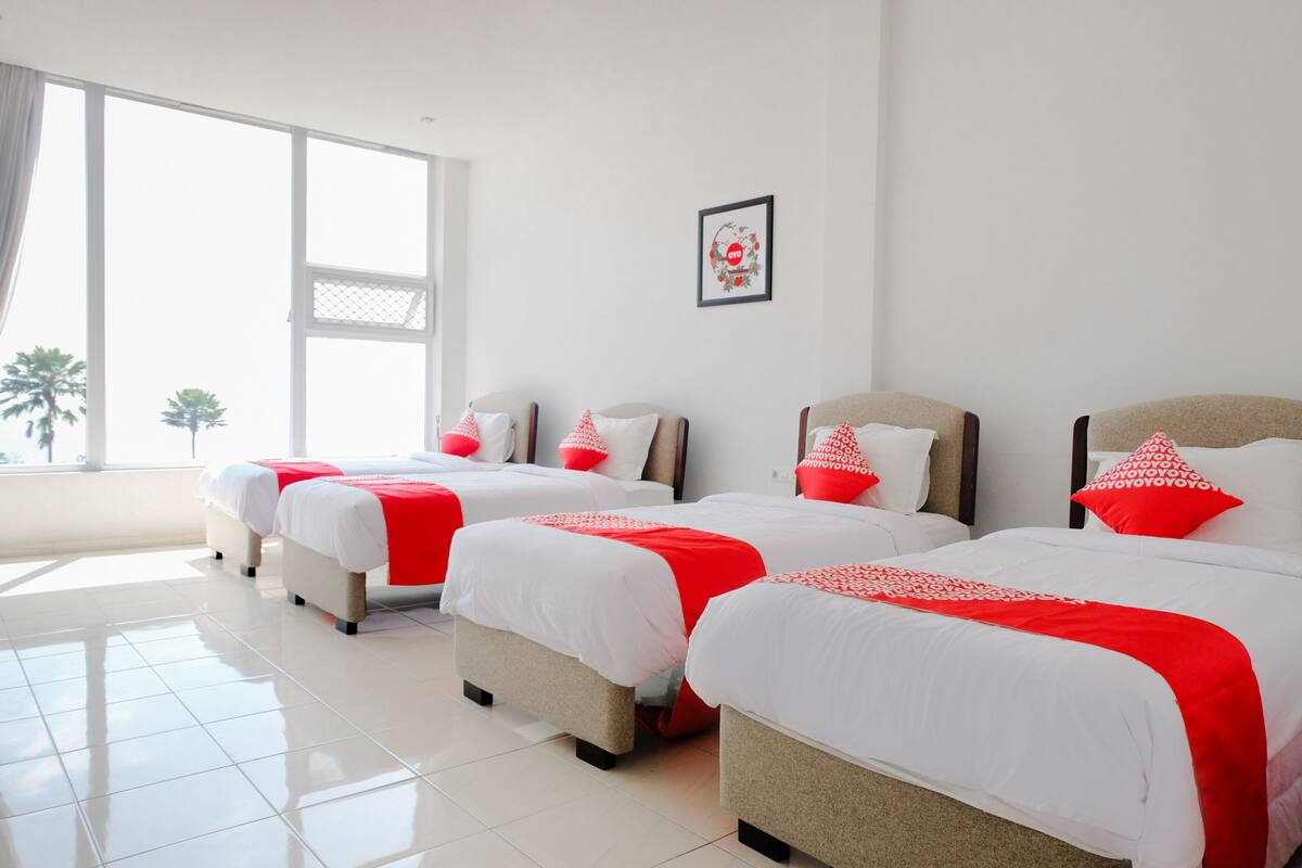 Une chambre d’hôtel avec trois lits, chacun agrémenté de draps blancs et de touches de couleur rouge.