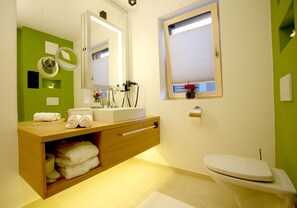 A modern bathroom with a wooden vanity, a toilet, and a window with blinds. - MountainVita (Untertauern)
