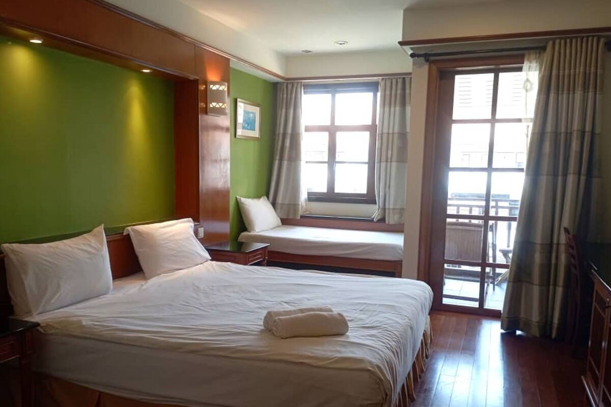 Quarto de hotel com uma cama grande, uma cama menor, uma janela com cortinas e vista para o exterior.