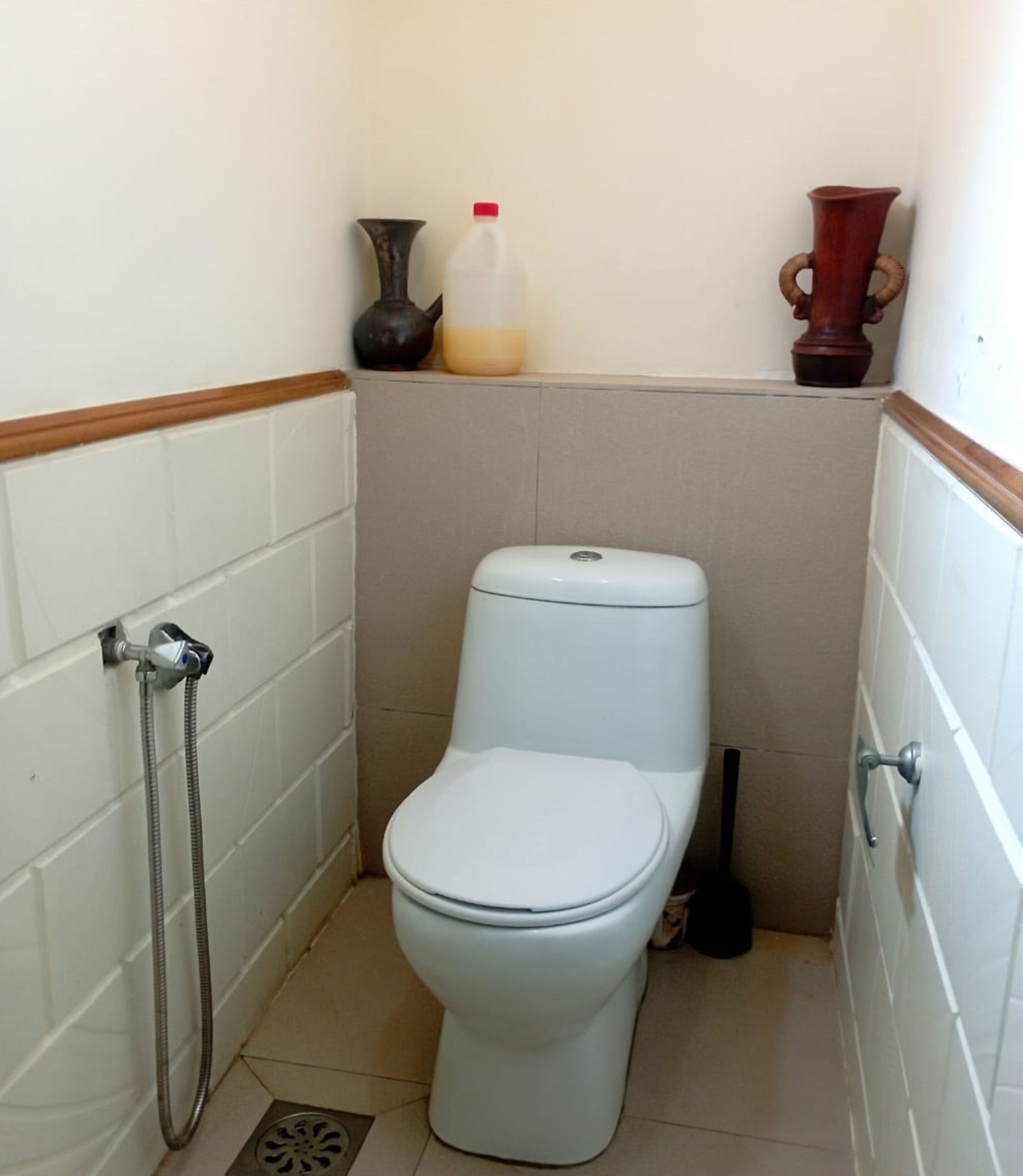 A small, white-tiled bathroom with a toilet, a shower, and a hand dryer.