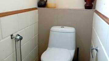 A small, white-tiled bathroom with a toilet, a shower, and a hand dryer.