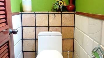 Een kleine badkamer met een toilet, een toiletborstel en een vaas met bloemen aan de muur.