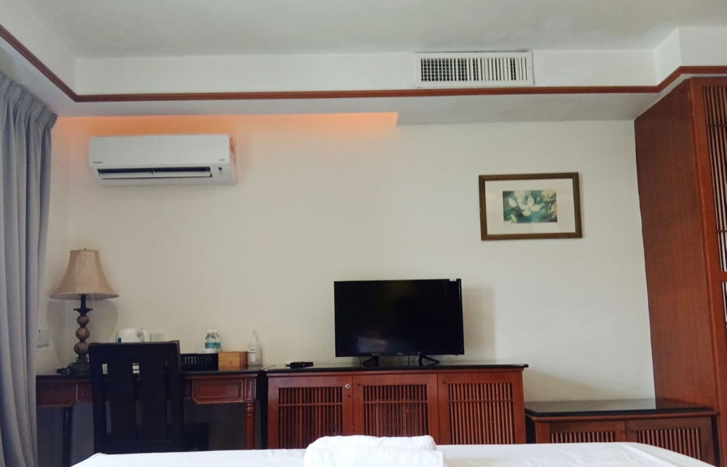 Una habitación de hotel con una cama, un escritorio con lámpara, un televisor, aire acondicionado y un cuadro en la pared.