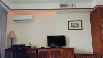 Una habitación de hotel con una cama, un escritorio con lámpara, un televisor, aire acondicionado y un cuadro en la pared.
